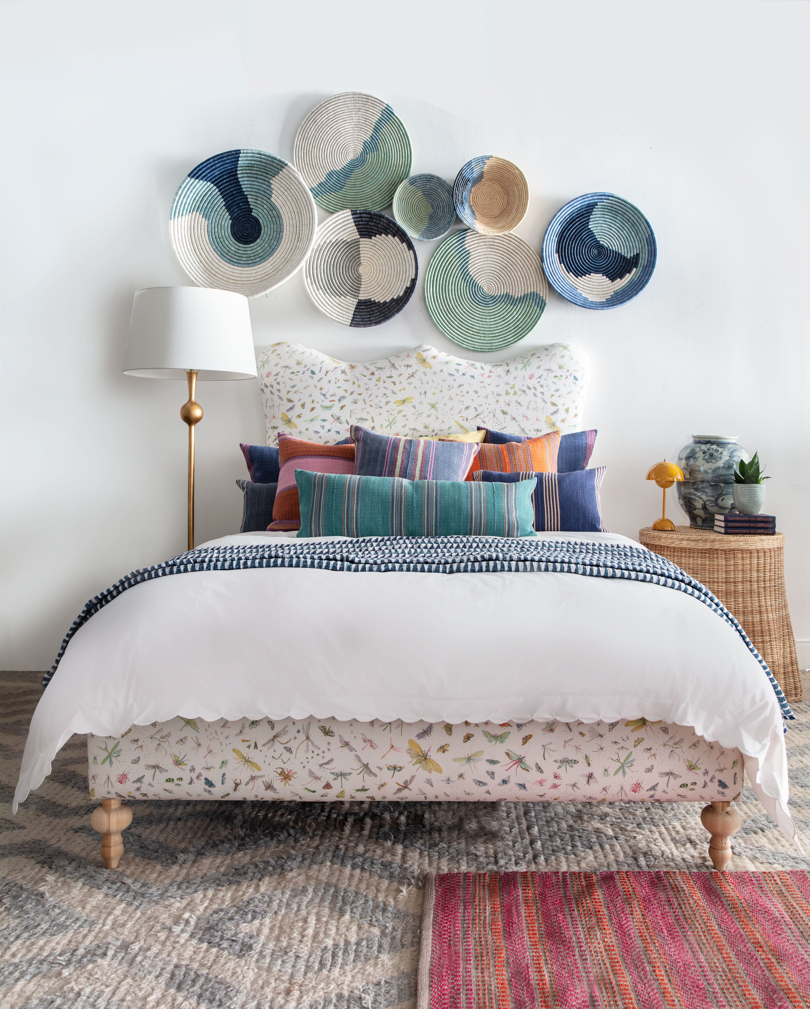 upholstered bed dressed with white duvet and striped pillows, blue and white baskets on wall