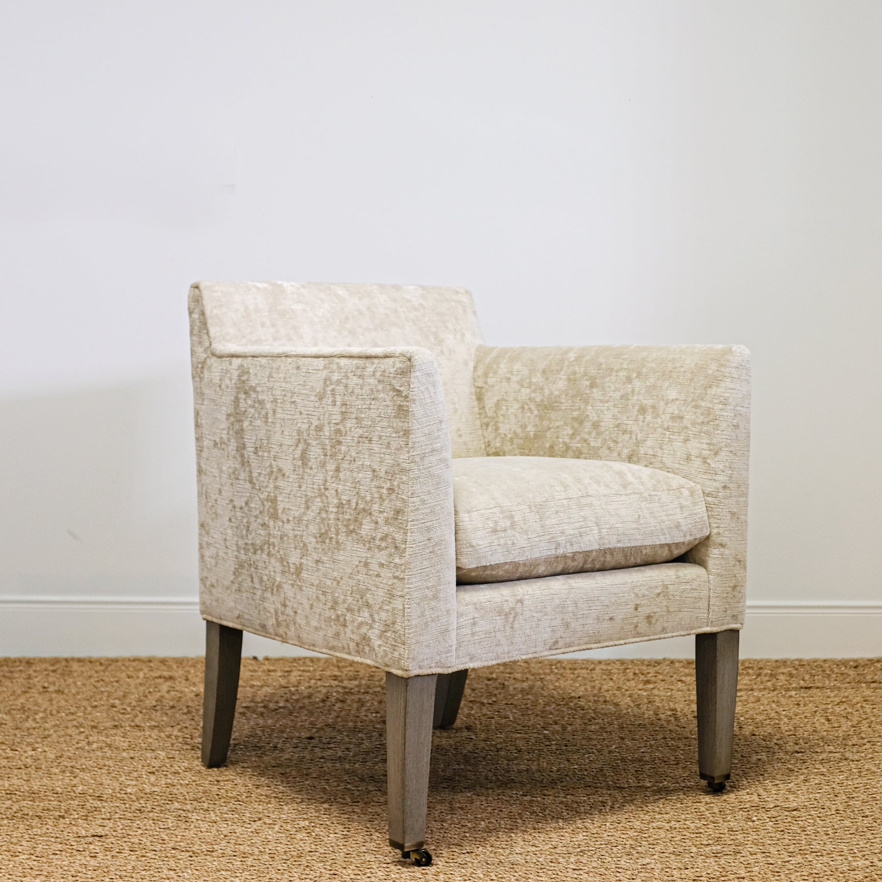 upholstered chair in mottled beige velvet with exposed wood leg, casters on front legs