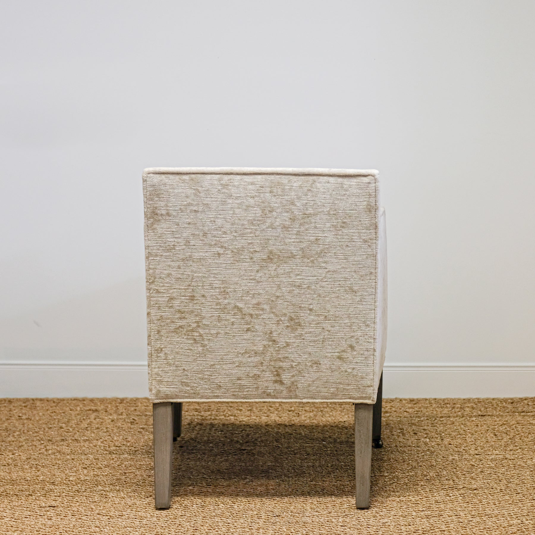 back view of upholstered chair in mottled beige velvet with exposed wood legs