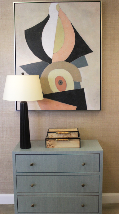 Gray dresser with abstract art above, lamp to the left, and books on top.
