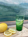 green moroccan drinking glass with sliced lemon in front of painting
