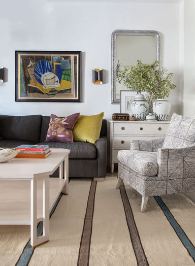 living room setting with grey sofa, striped rug, brown and white chair and white cocktail table