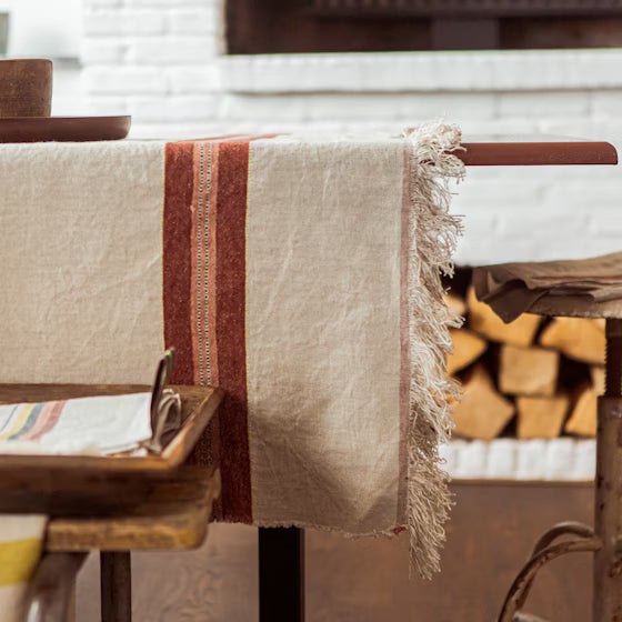 Beige tablecloth with brown stripes on a wooden table in a rustic setting.