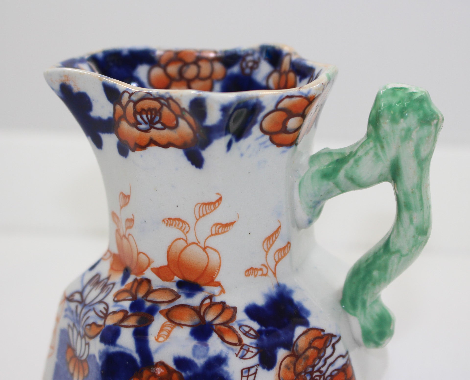 Ceramic pitcher with floral patterns and a green handle on a white background