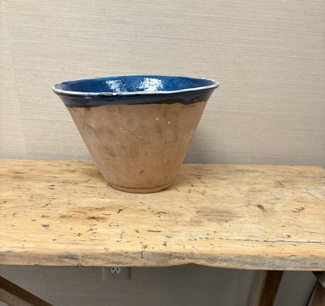 Large ceramic bowl with blue interior on a wooden table against a beige wall.