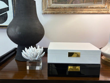 Decorative box with gold accents on a table next to a black vase and white coral sculpture.