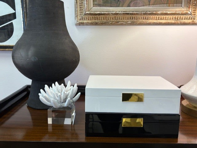 Decorative box with gold accents on a table next to a black vase and white coral sculpture.