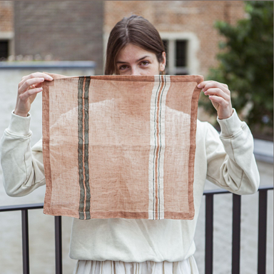 Young lady holding up old rose Mojave linen napkin from Libeco to show sheerness