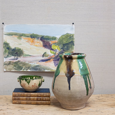 terra cotta pot with dripping glaze in front of watercolor artwork and beside a stack of books