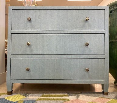 Light blue dresser with three drawers and brass knobs on a patterned rug.