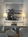 A large black and white framed art print depicting a woman on a vintage motorcycle by the beach, displayed on a console table in a styled room setting with two table lamps and ceramic vases.