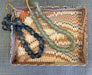Two beaded strands draped over a decorative marbled tray: one strand consists of dark navy blue beads, and the other consists of translucent pale green-gray beads. The tray features a cream, orange, and brown marbled pattern and is placed on a gray textured fabric background.
