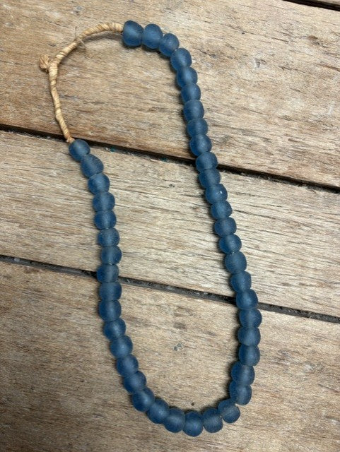 A strand of matte dark blue-gray round beads with a natural tan cord closure, laid on a rustic wooden surface.