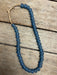 A strand of matte dark blue-gray round beads with a natural tan cord closure, laid on a rustic wooden surface.