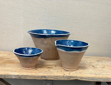Three ceramic bowls with blue interior on a wooden table against a beige wall.