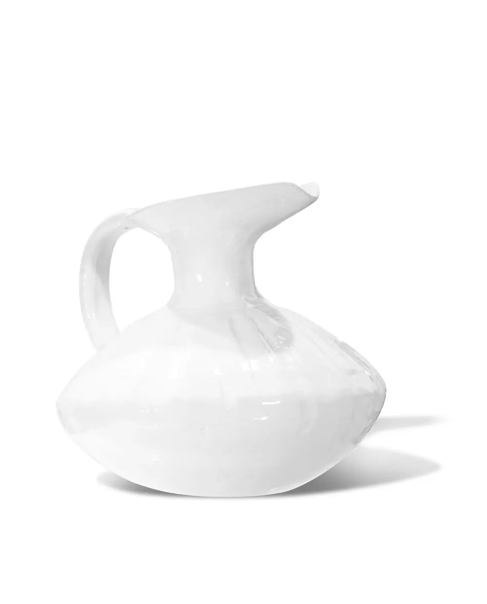 A glossy white ceramic pitcher with a rounded body, curved handle, and short spout, photographed on a clean white background with a soft shadow.