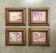 Four framed landscape art prints arranged in a 2x2 grid on a textured gray wall. Each print features a purple-toned scenic illustration with an ornate gold-toned frame.