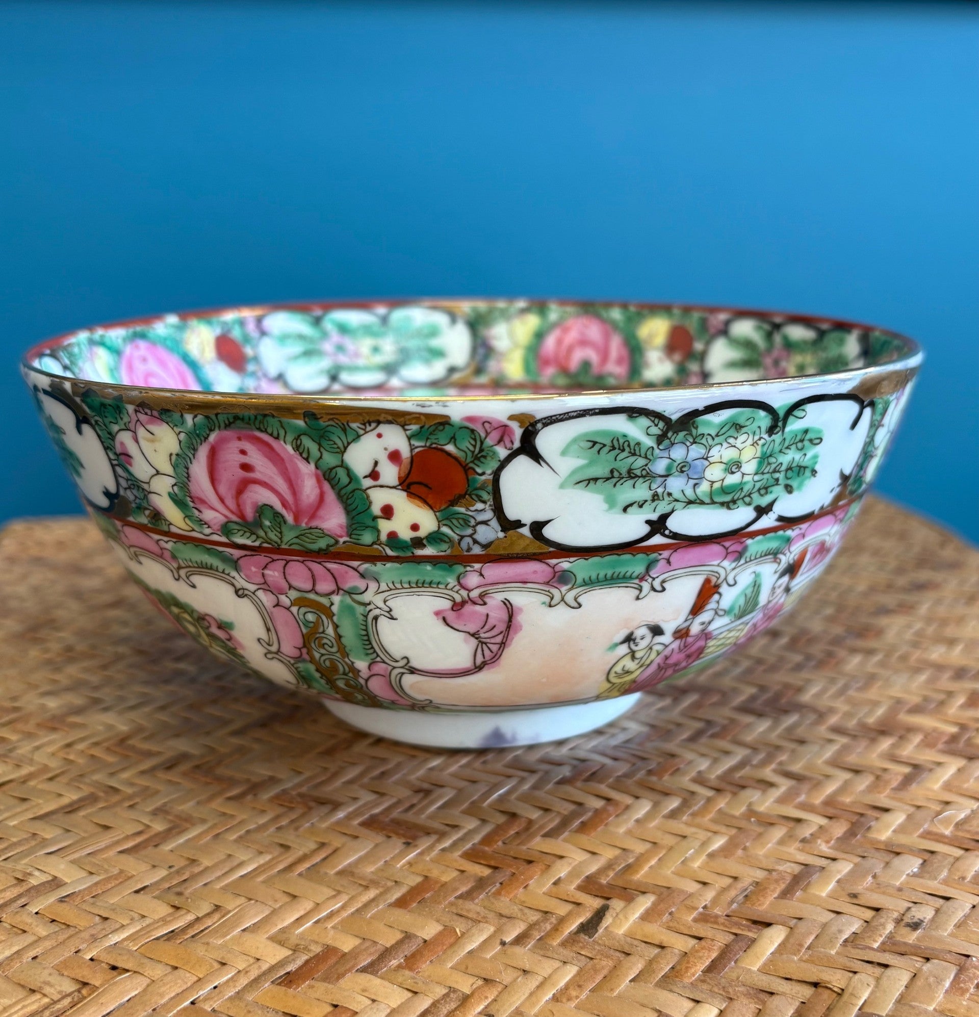 Decorative ceramic bowl with colorful floral and animal patterns on a woven surface with blue background