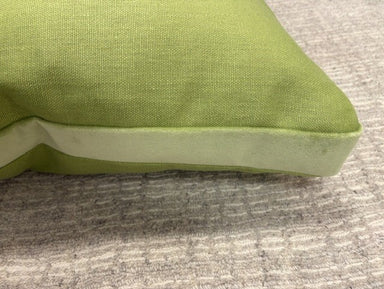 A close-up of a lime green throw pillow with a contrasting light sage green piping border, resting on a textured gray carpet.