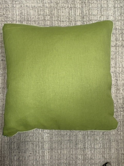 A square leaf green throw pillow with piped edges, resting on a textured gray woven rug.
