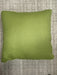 A square leaf green throw pillow with piped edges, resting on a textured gray woven rug.
