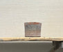 Small terra cotta pot on a wooden plank against a textured beige wall