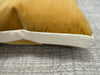 A close-up of a butterscotch yellow velvet throw pillow with a contrasting white fabric trim, resting on a textured gray carpet.