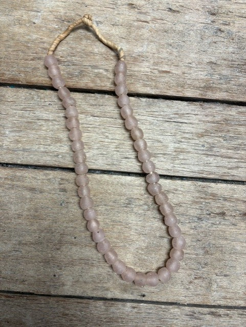 A single strand of pale pink faceted beads with a knotted tan cord, laid on a rustic weathered wood surface.