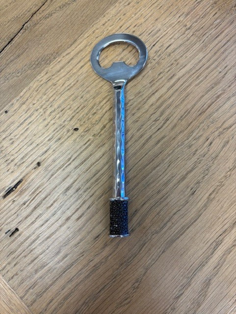 Metal bottle opener with black grip on a wooden surface