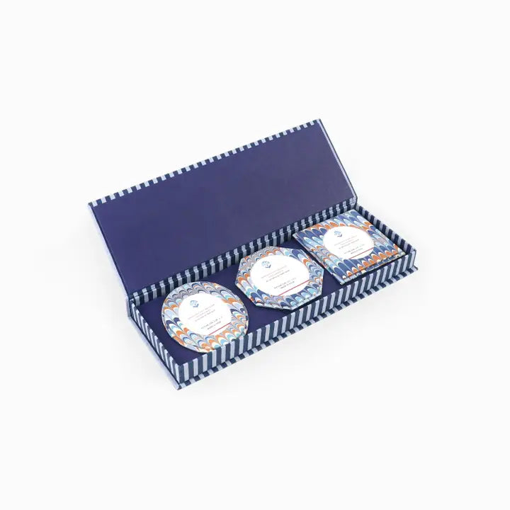 A navy blue gift box with a striped border, open to reveal three round frames with blue and orange marble patterns and white labels, set against a plain white background.