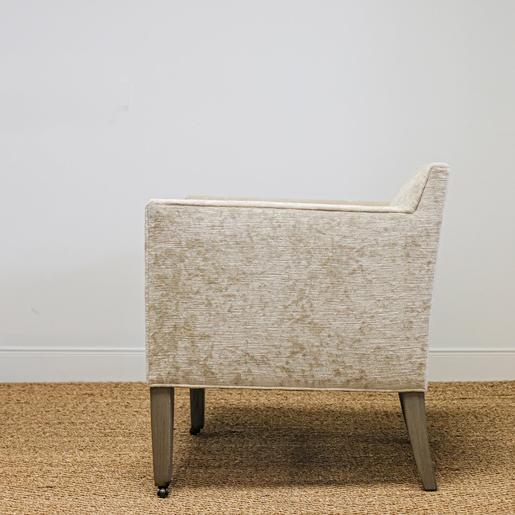 upholstered chair in mottled beige velvet with exposed wood leg, casters on front legs