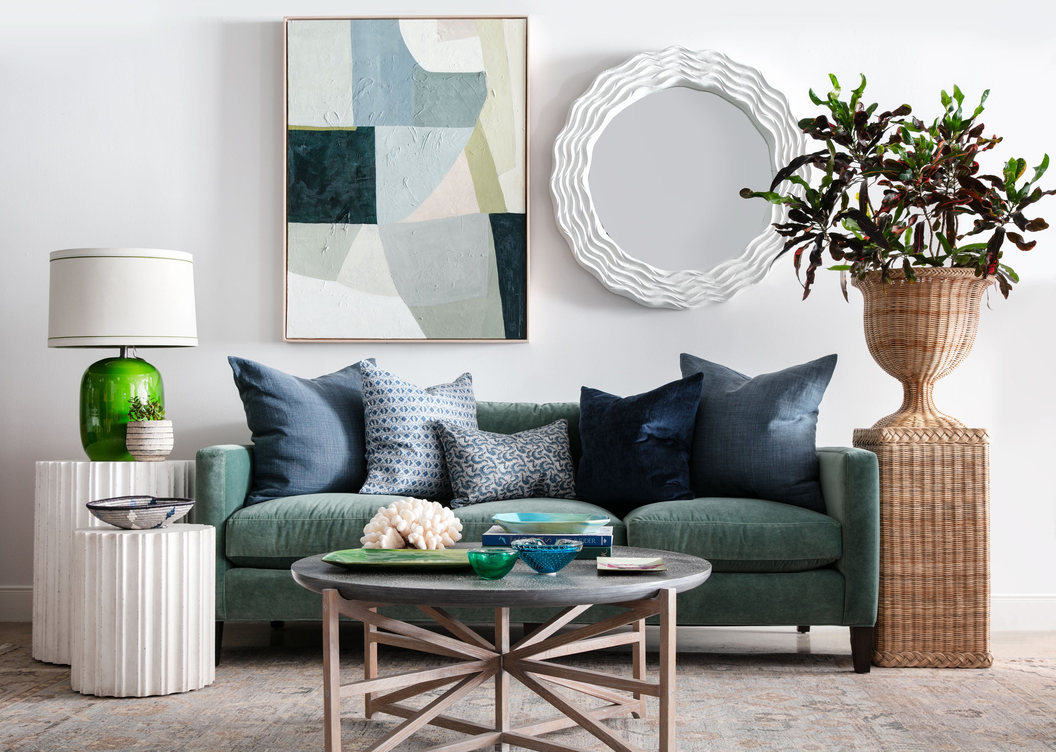 green sofa with rug, round cocktail table, side tables, round mirror and abstract art hanging above