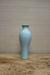 Light blue ceramic vase on a wooden surface with a beige wall background