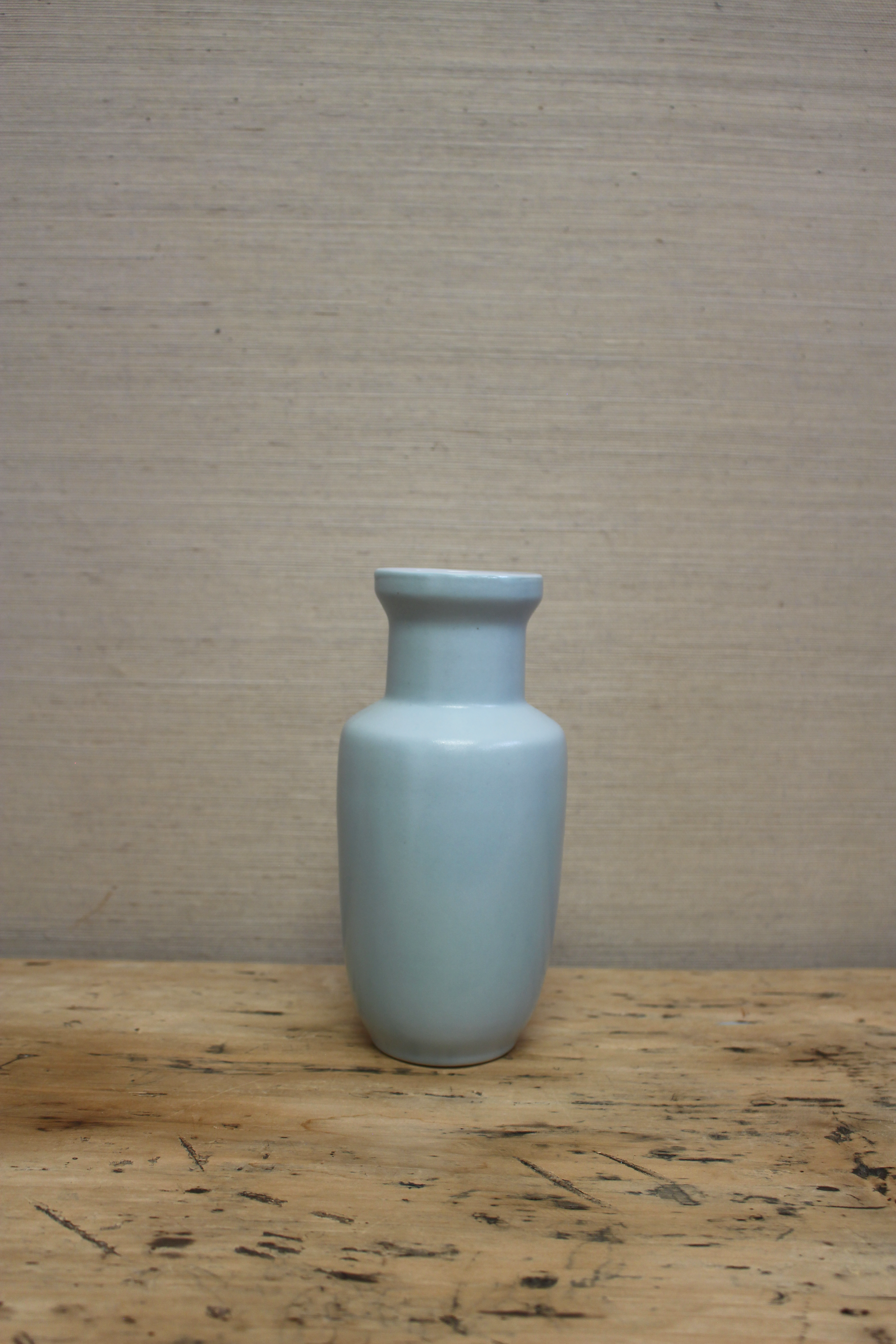 Light blue ceramic vase on a wooden surface with a beige wall background