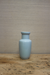 Light blue ceramic vase on a wooden surface with a beige wall background