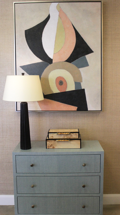 Gray dresser with abstract art above, lamp to the left, and books on top.