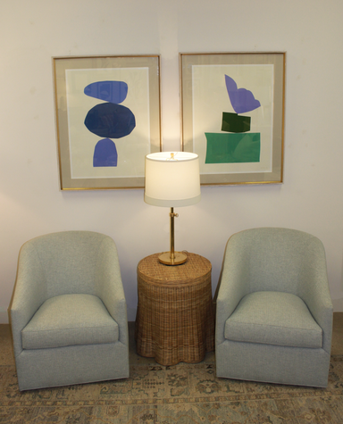 Two armchairs flanking a lamp on a wicker side table with abstract art on the wall.