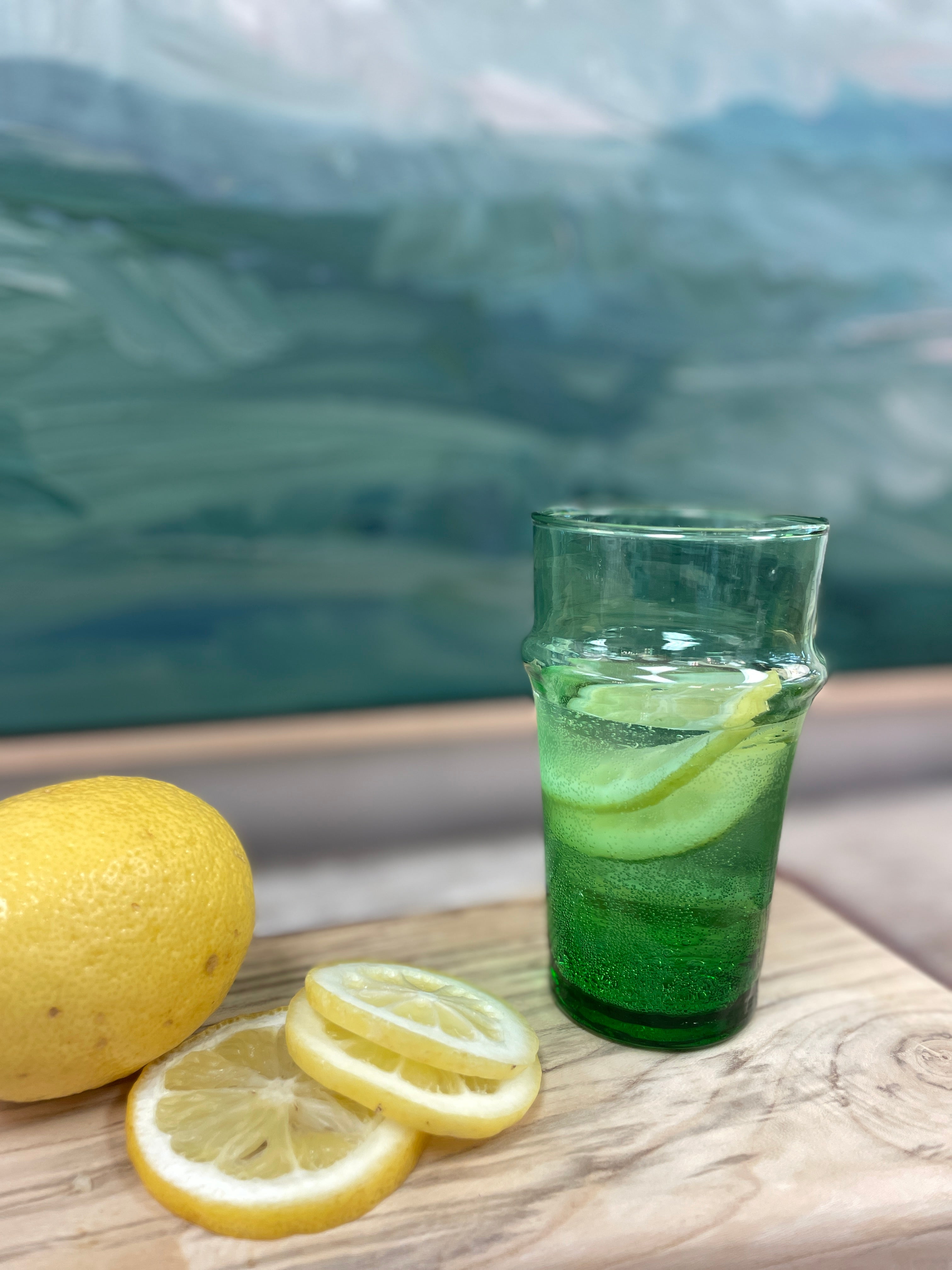 green moroccan drinking glass with sliced lemon in front of painting