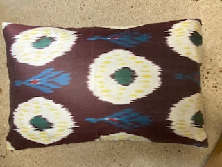 A square-shaped decorative pillow with a geometric ikat pattern in purple, blue, and beige colors.