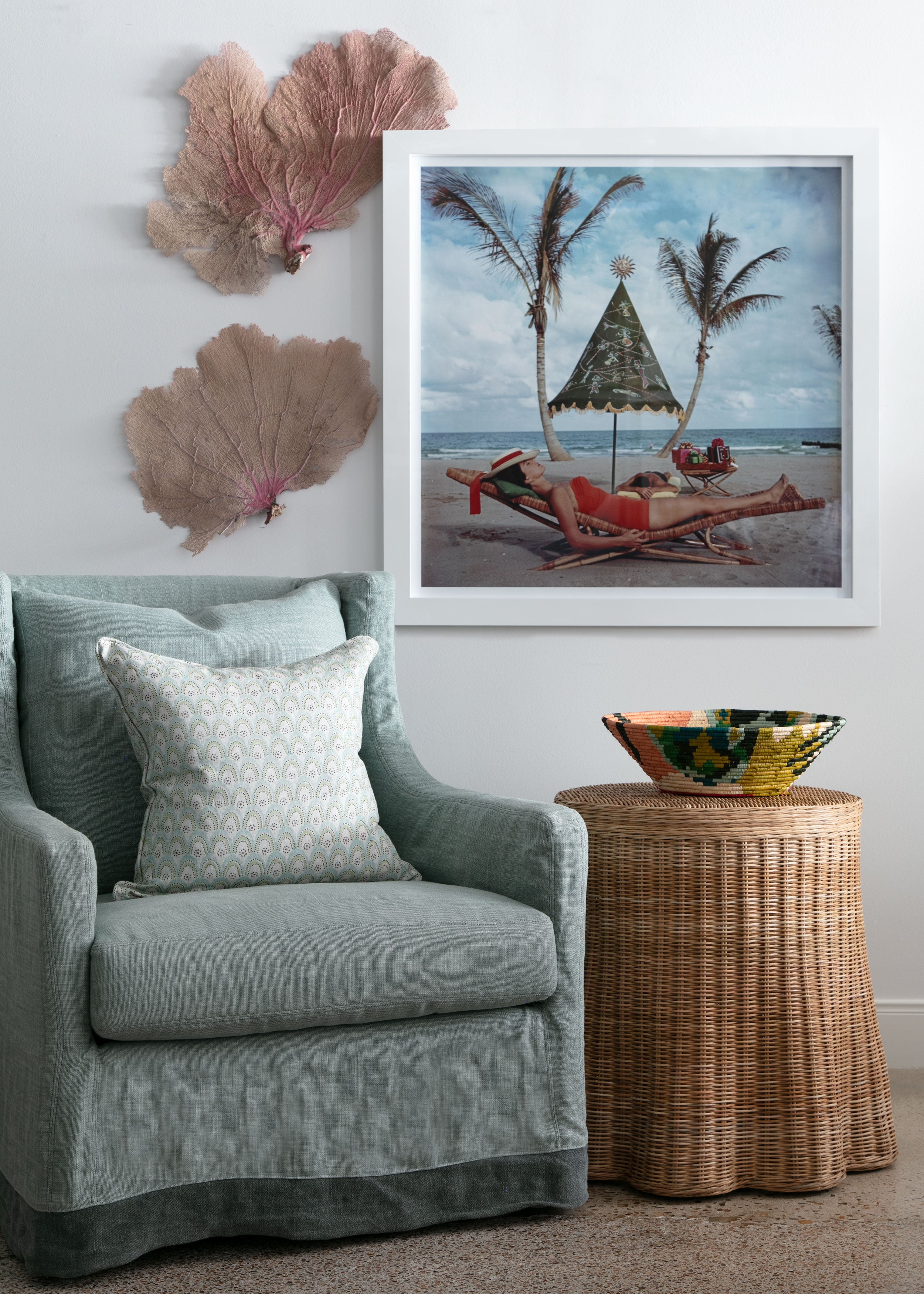 linen slipcovered chair beneath framed photograph and wicker side table, sea fans on wall