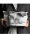 A person in a dark blazer holds a large, sculptural white ceramic vessel with a highly organic, wavy, crumpled surface texture.