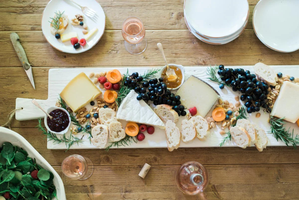 Wooden table with a cheeseboard, fruits, and glasses on a wooden surface