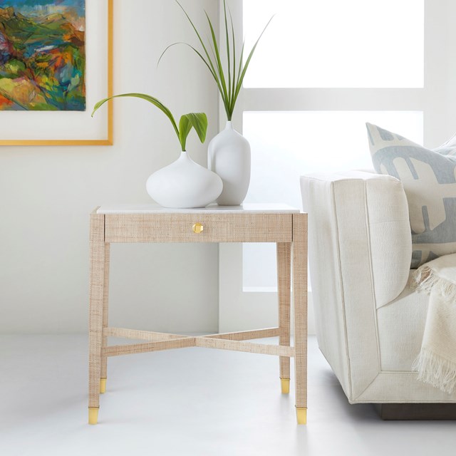 Beige side table with white vases and green plants in a living room setting.