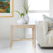 Beige side table with white vases and green plants in a living room setting.