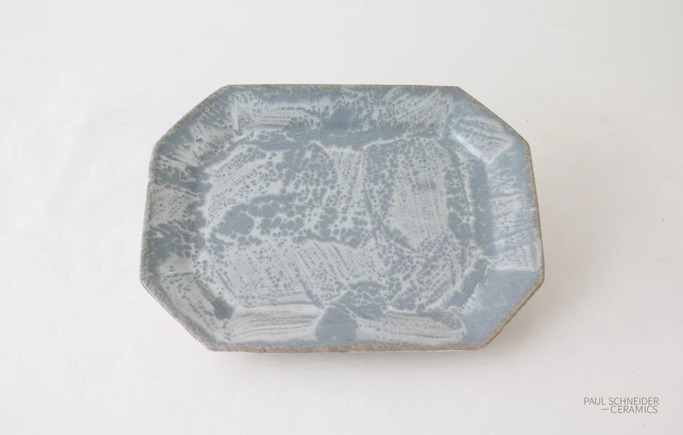 An octagonal ceramic plate with a textured, mottled blue and white glaze, photographed from a top-down angle on a white background.