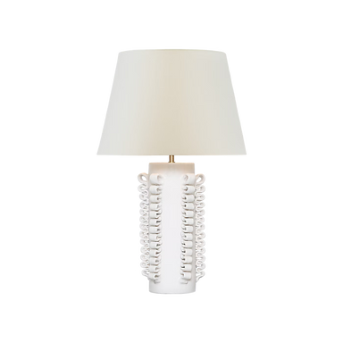 A table lamp with a tapered off-white fabric shade and a sculptural white ceramic base featuring vertical loops and a small gold-toned accent at the top, shown on a plain white background.