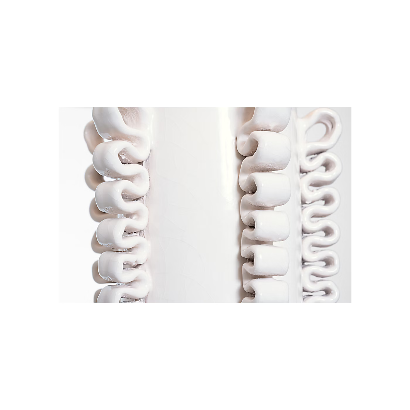 A close-up studio shot of a white textured product with repeating curved, looped segments arranged vertically on a white background.