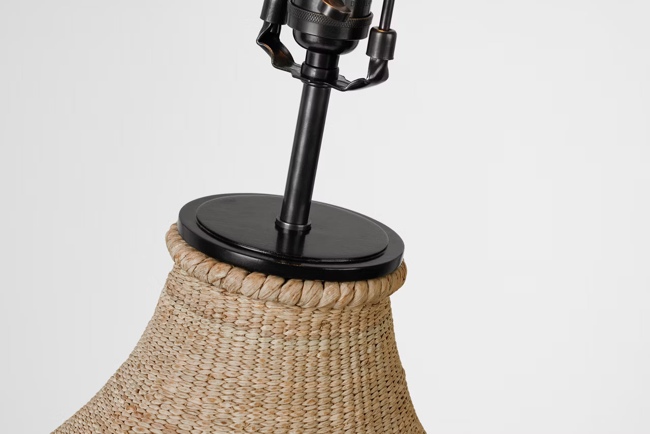 Close-up of a woven natural-fiber lampshade with a black metal neck and round top cap, shown against a plain light gray background.