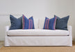 white sofa with four pillows, two solid blue and two blue and pink stripe