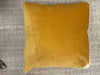 A square butterscotch yellow velvet throw pillow with a white piped edge, resting on a textured gray fabric background.